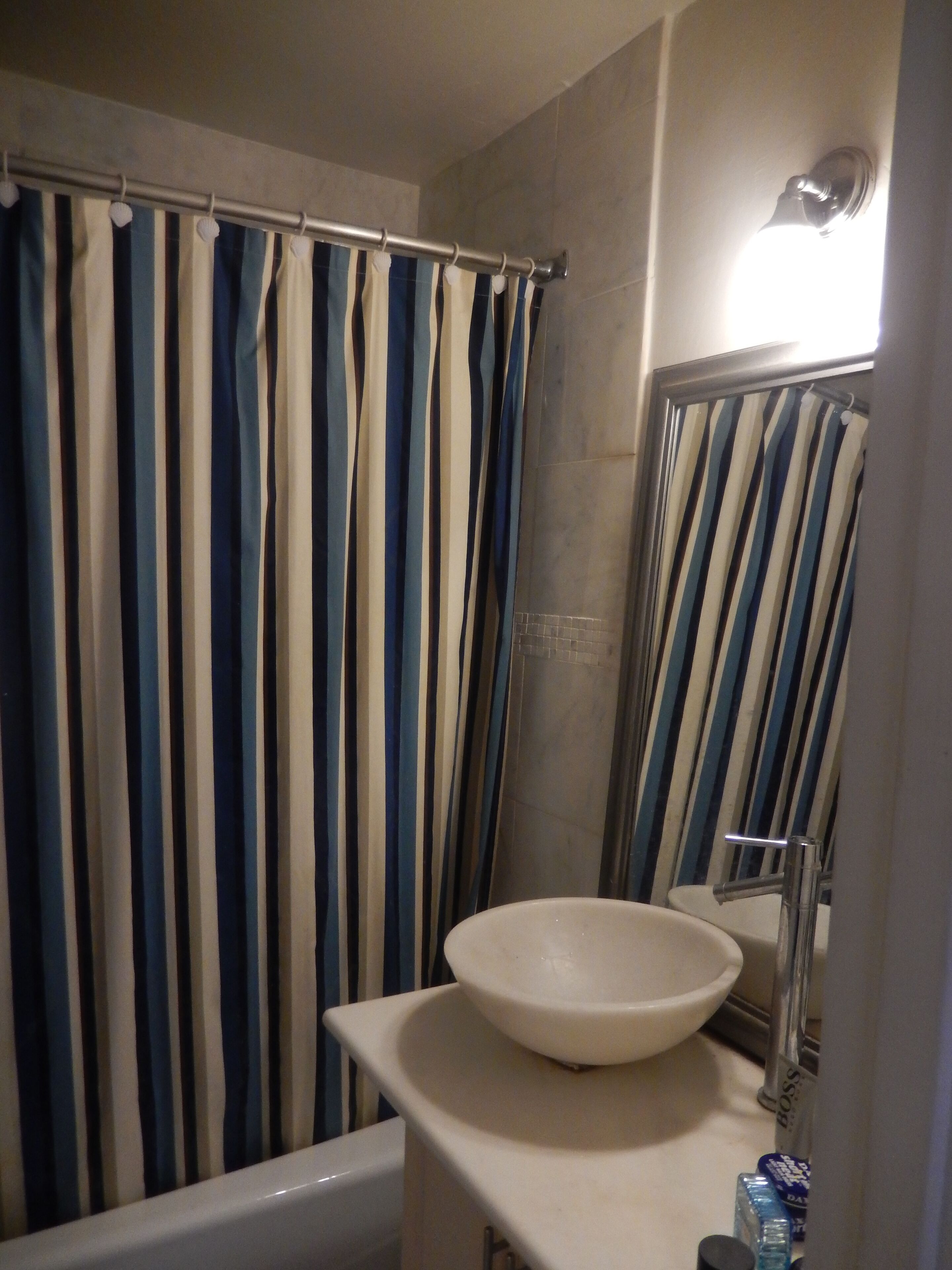 A bathroom with a bathtub, a sink with a vessel basin, a striped shower curtain, and a mirror.