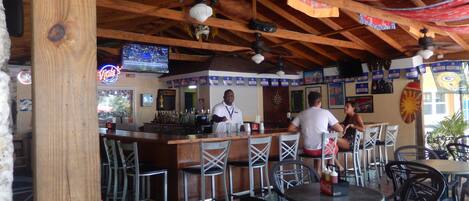 An indoor restaurant with wooden beams, a bar area, and tables and chairs.