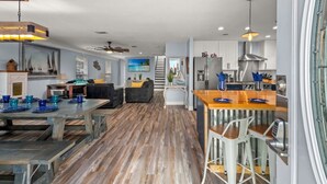 Un vaste espace de vie doté d’un plancher en bois, d’une table à manger dressée avec de l’assiette bleue et d’une cuisine équipée d’appareils modernes et de tabourets de bar.