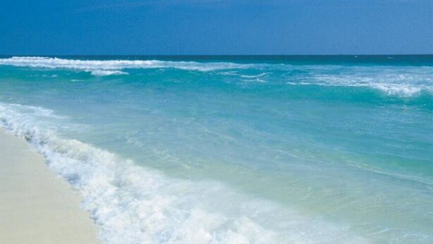 Une plage à l’eau d’un bleu limpide et au sable blanc.