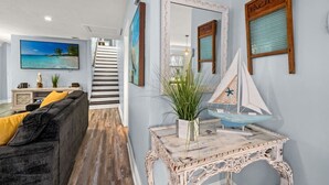 Un salon comprenant un canapé, une console sur laquelle est posé un modèle de voilier, et un escalier menant à une autre pièce.