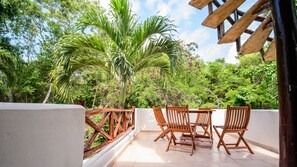 Relax on the balcony with a view of lush greenery and a tall palm tree, featuring a table and chairs for a peaceful retreat.