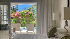 Une chambre d’hôtel avec un lit, une table de chevet, une lampe et une vue sur une piscine et un jardin.