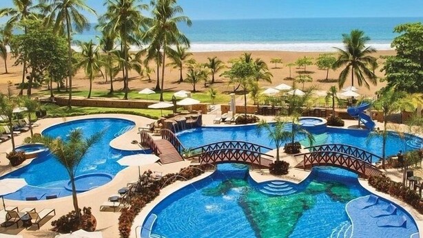 A resort with multiple swimming pools, palm trees, and a beach view. - Oceanfront  Beachfront Condo Vacational Rental Jacó Beach Playa Jacó, costa rica (Garabito)