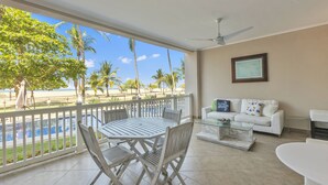 A balcony with a view of the beach and pool, a white sofa, and a dining table with chairs. - Oceanfront  Beachfront Condo Vacational Rental Jacó Beach Playa Jacó, costa rica (Garabito)