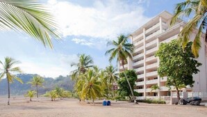 A beachfront hotel with multiple balconies, palm trees, and a sandy beach. - Oceanfront  Beachfront Condo Vacational Rental Jacó Beach Playa Jacó, costa rica (Garabito)