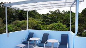 A covered outdoor seating area with blue cushioned chairs and white tables, surrounded by lush greenery. - Oasis in Downtown next to Simon Bolivar Park with private balcony (San José)
