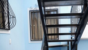 A staircase with black railings leading to a landing with a window. The walls are painted blue, and the floor has patterned tiles. - Oasis in Downtown next to Simon Bolivar Park with private balcony (San José)