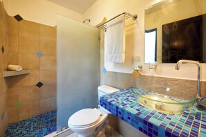 A bathroom with a glass bowl sink, a white toilet, and a shower area with patterned tiles.