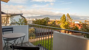 Un balcon avec une table et des chaises, offrant une vue sur la ville et les montagnes qui se dessinent à l’horizon.