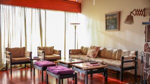 Un salon comprenant un canapé, deux fauteuils, une table basse et un banc. On y trouve également un lampadaire et un tableau accroché au mur.