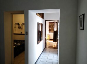 A hallway with a bed, a mirror, a clock, and a door leading to another room.