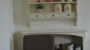 Une table à manger est dressée avec des assiettes, des bols, des verres à vin et des couverts. Au-dessus de la table, on trouve une étagère blanche où sont disposés des objets décoratifs et des boîtes de rangement.