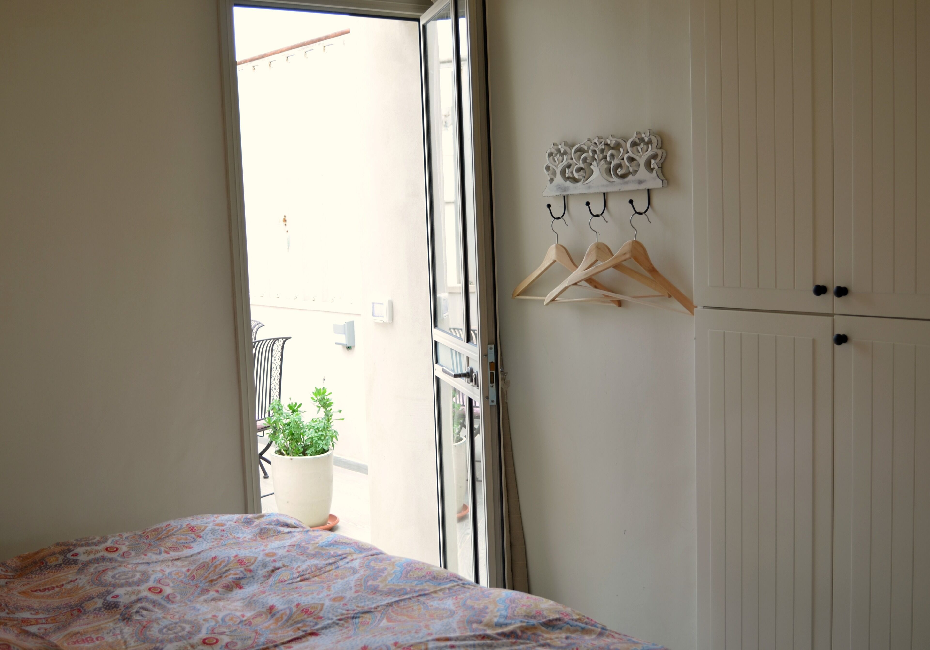 Un dormitorio con cama, planta en maceta, armario y puerta que da a un área exterior.