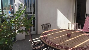Une terrasse ensoleillée avec une table ronde, des chaises et un pot de fleurs.