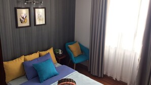 Une chambre à coucher avec un lit, deux tableaux encadrés, une chaise et une fenêtre avec des rideaux.