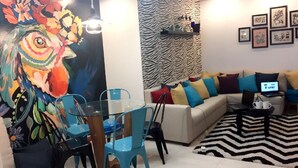 Un salon moderne avec une table à manger en verre, des chaises colorées, un canapé agrémenté de coussins à motifs et un tapis à rayures zébrées.