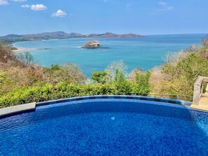 Une piscine d’eau cristalline, d’un bleu éclatant, offrant une vue sur l’océan et les collines lointaines.
