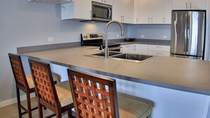 Une cuisine moderne dotée d’un grand îlot central, d’appareils électroménagers en acier inoxydable et de chaises en bois.