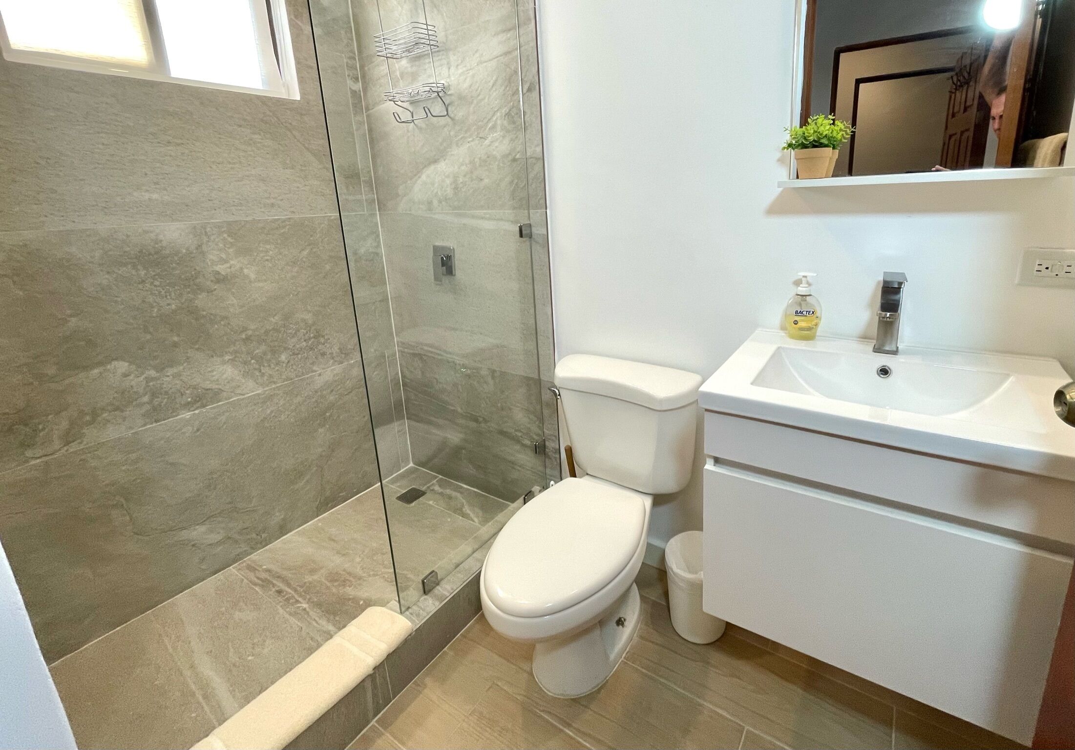 Un bany modern amb dutxa tancada per vidre, un vàter blanc i un lavabo amb un mirall a la part superior.