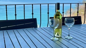 Une table avec une bouteille et deux verres, placée sur un balcon donnant sur la mer.
