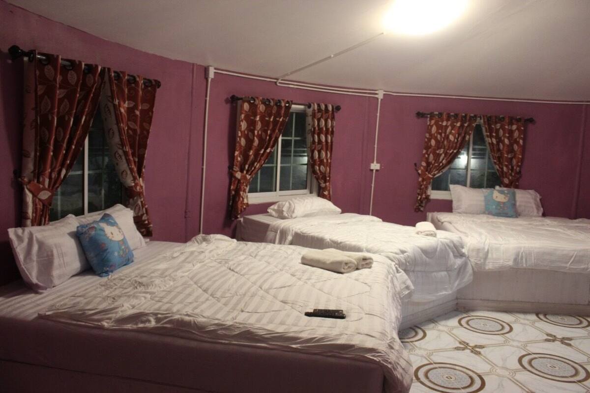 A room with three beds, purple walls, and patterned curtains.