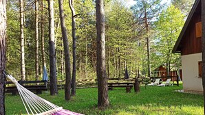 Un hamac dans une zone herbeuse, avec une cabane en bois et des tables de pique-nique en arrière-plan.