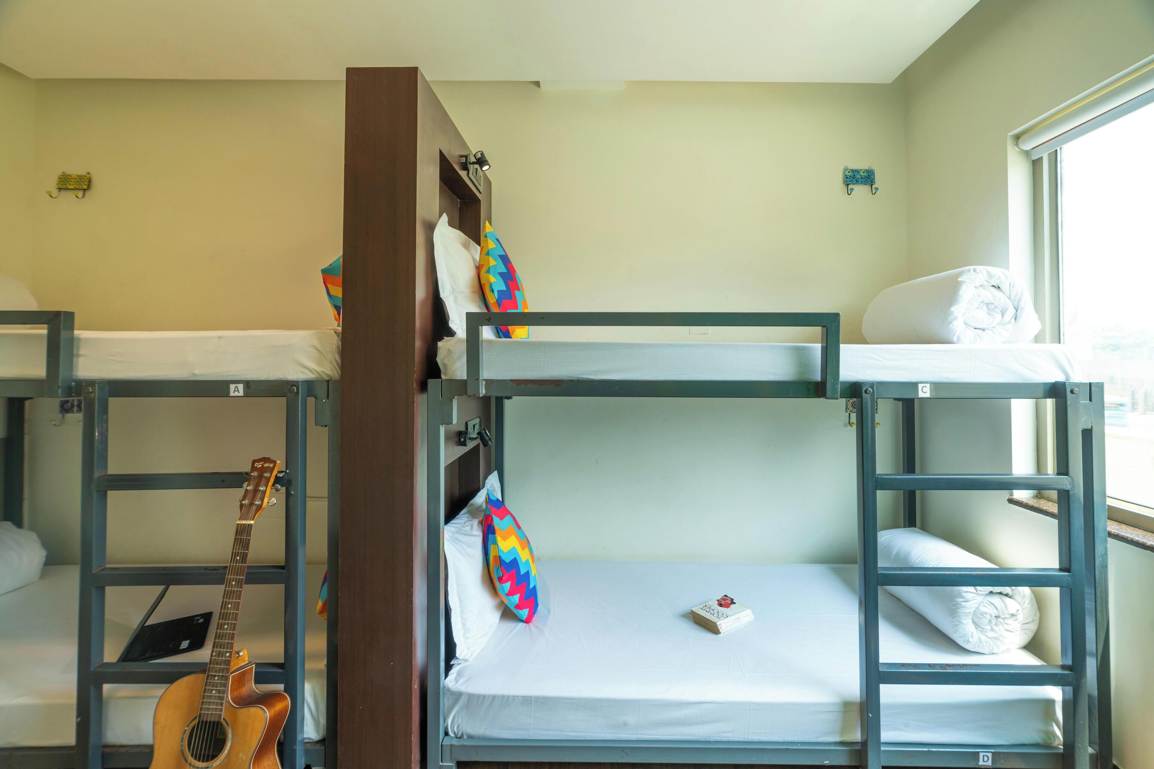 A bunk bed room with a guitar, colorful pillows, and a window.