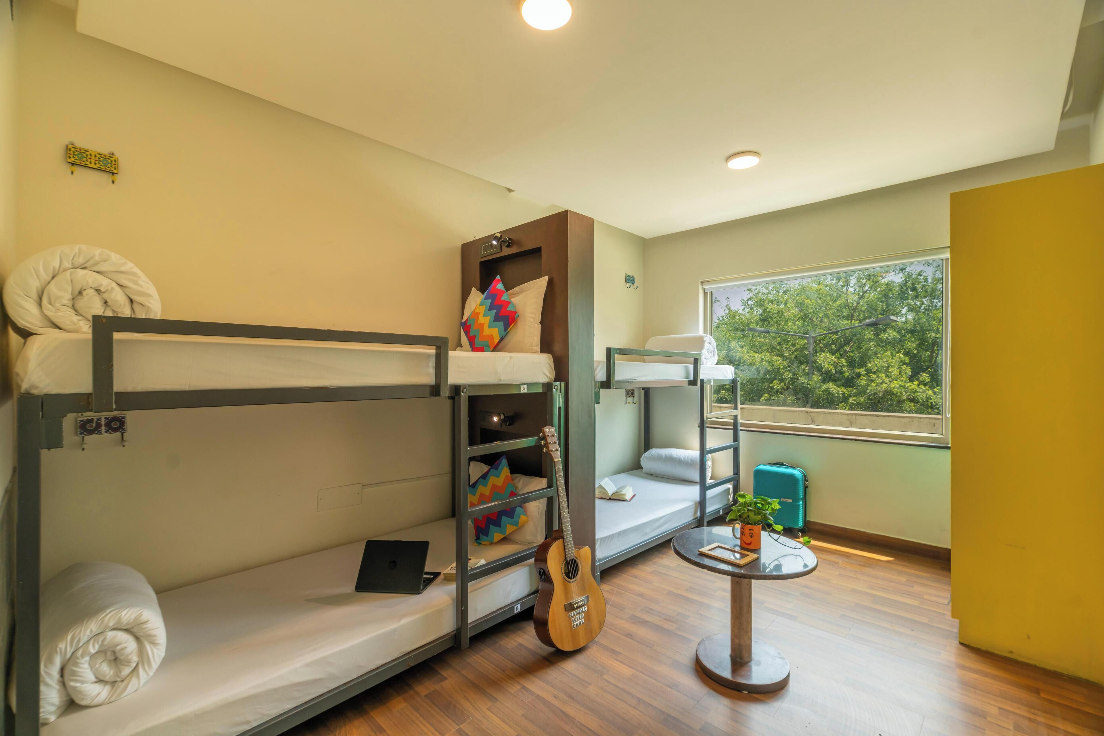 Dormitorio con literas, una guitarra, una mesita con una planta y una ventana con vistas a árboles.
