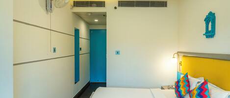 A hotel room with a bed, a bedside table, a wall-mounted fan, a door, and a light fixture.