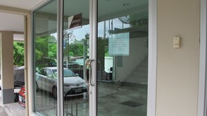 A glass door entrance with a sign indicating "Entrance" and a parking area with cars visible. - AP Apartment (Si Racha)