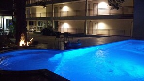 Una piscina de color azul, rodeada por un edificio con varios balcones y un área de estacionamiento.