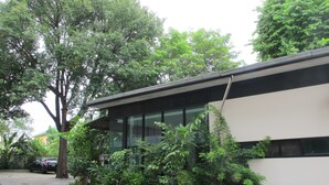 A modern building with large windows, surrounded by lush greenery and potted plants. - AP Apartment (Si Racha)