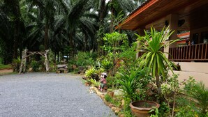 A gravel pathway leading to a wooden structure with a balcony, surrounded by lush greenery and various potted plants. - Tonpalm Farmstay (Khlong Thom)