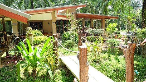 A tropical garden with a wooden bridge, a covered seating area, and lush greenery. - Tonpalm Farmstay (Khlong Thom)