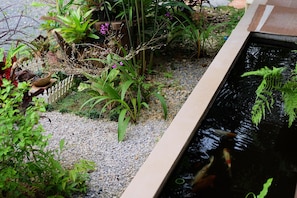 A koi pond with a wooden border, surrounded by gravel and various plants. - Tonpalm Farmstay (Khlong Thom)
