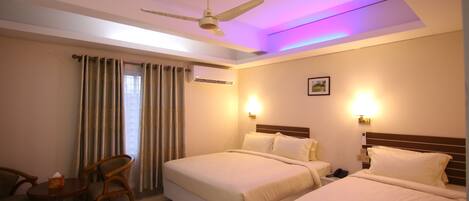 A hotel room with two beds, a ceiling fan, a table with chairs, and a window with curtains.