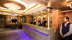 A hotel reception area with a marble counter, wooden paneling, a chandelier, and a flat-screen TV.