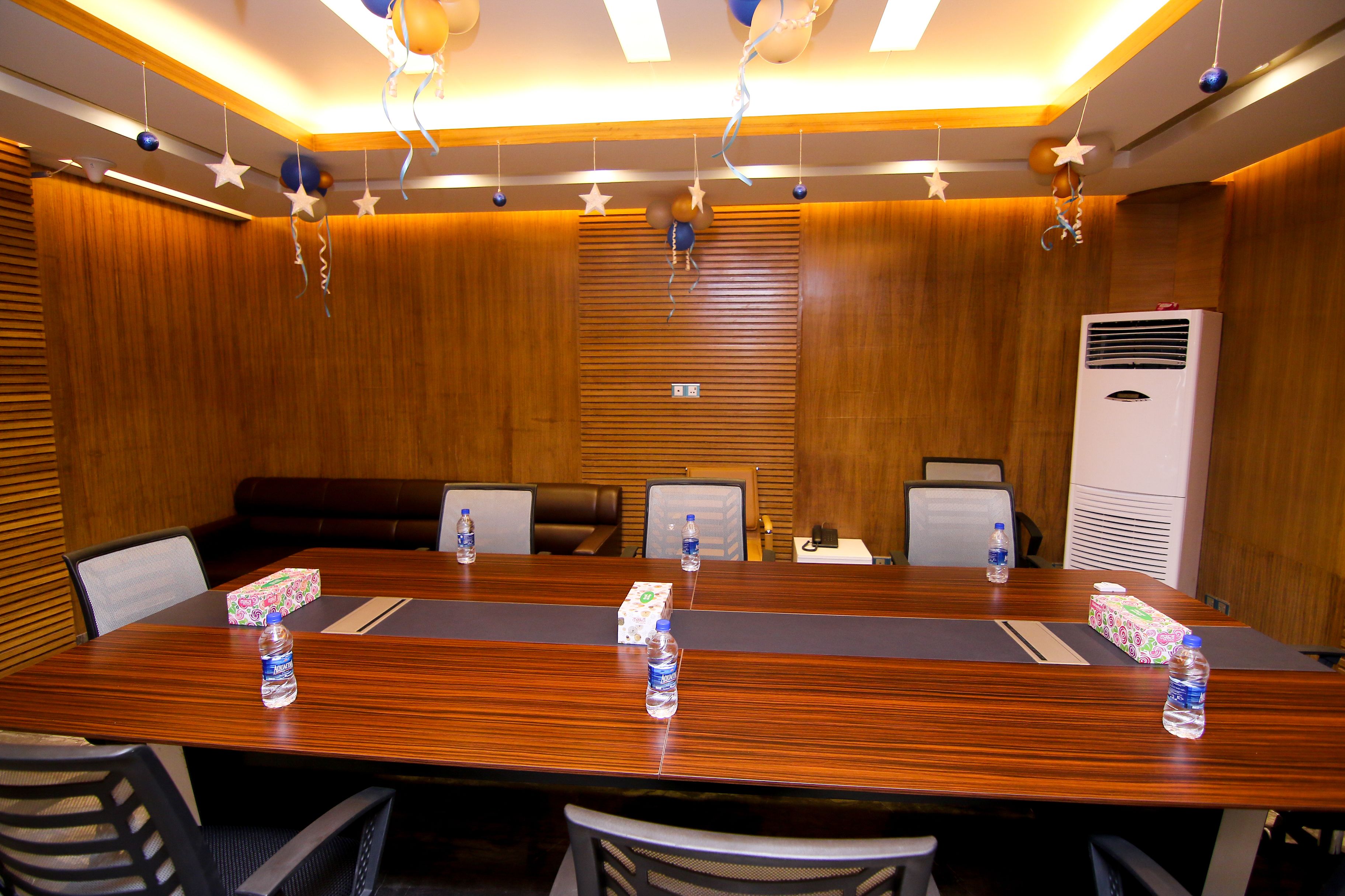 A conference room with a long wooden table, multiple chairs, and two air conditioning units.