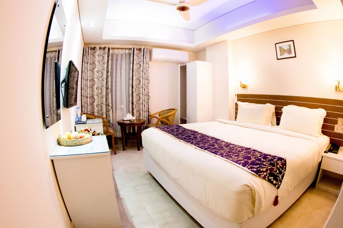 Habitación de hotel con cama, escritorio con silla, una mesita, televisor y ventilador de techo.