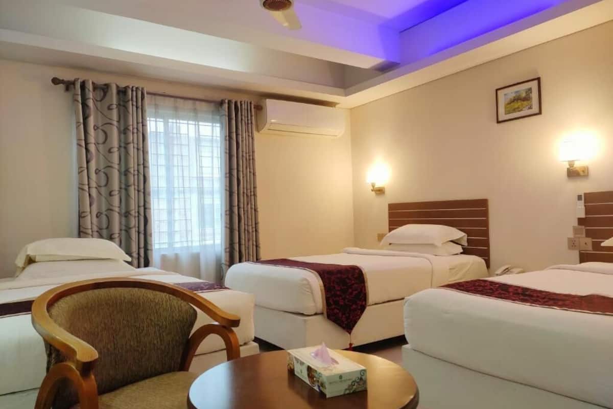 Habitación de hotel con dos camas, una silla, una mesa redonda y un ventilador de techo.