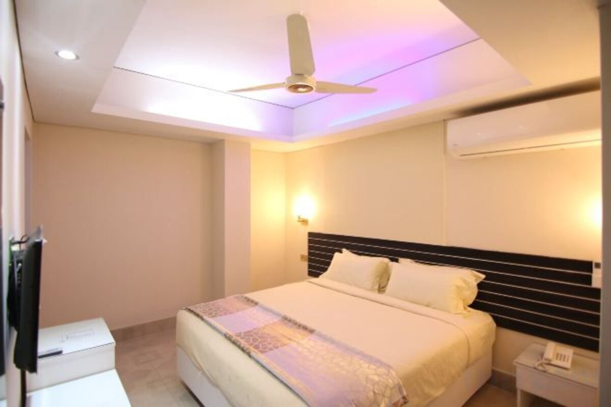 A hotel room with a bed, a ceiling fan, a bedside table, and a wall-mounted air conditioner.