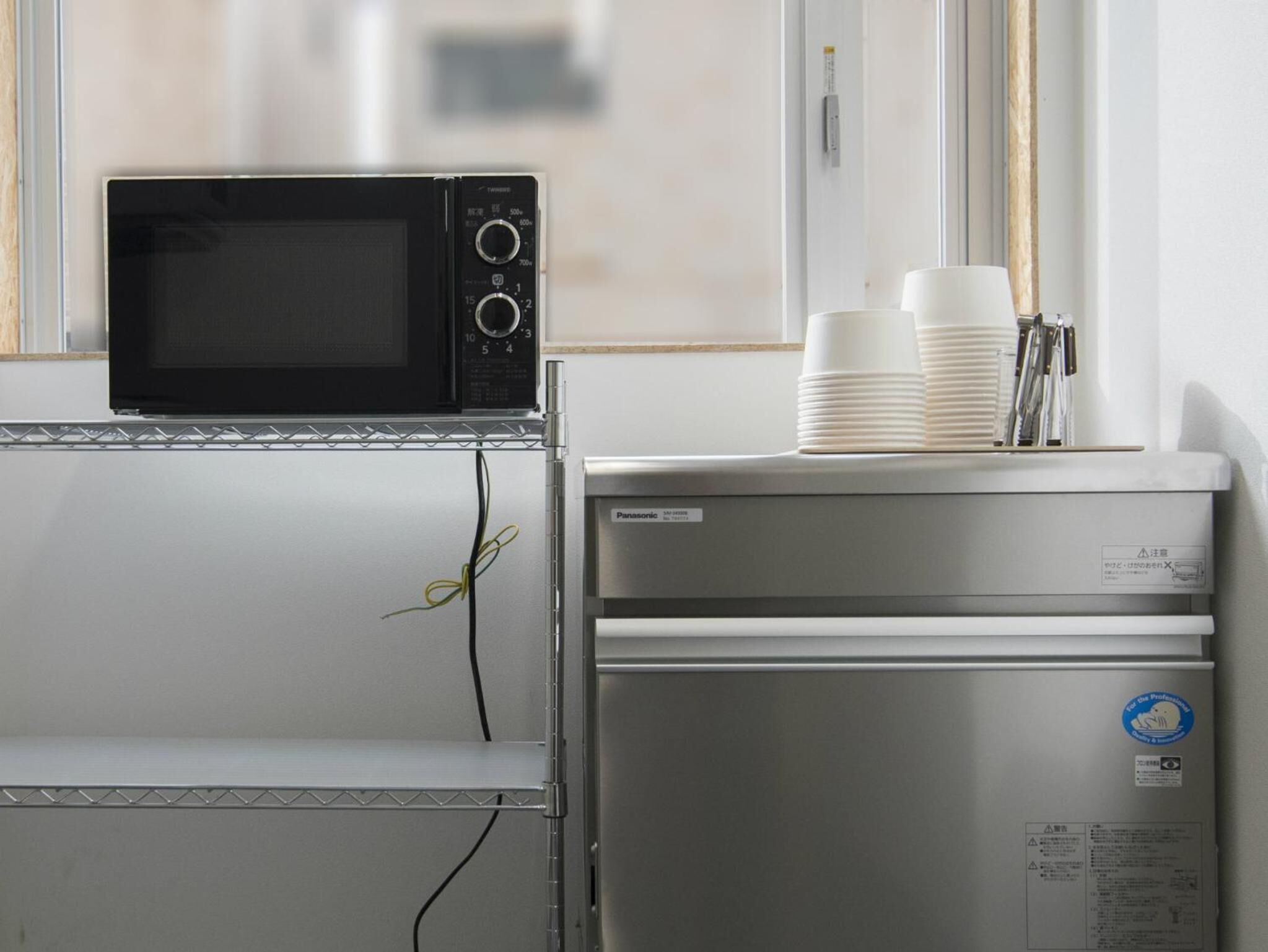 A kitchenette with a microwave, a small refrigerator, and a window with blinds.