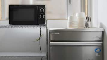 A kitchenette with a microwave, a small refrigerator, and a window with blinds.