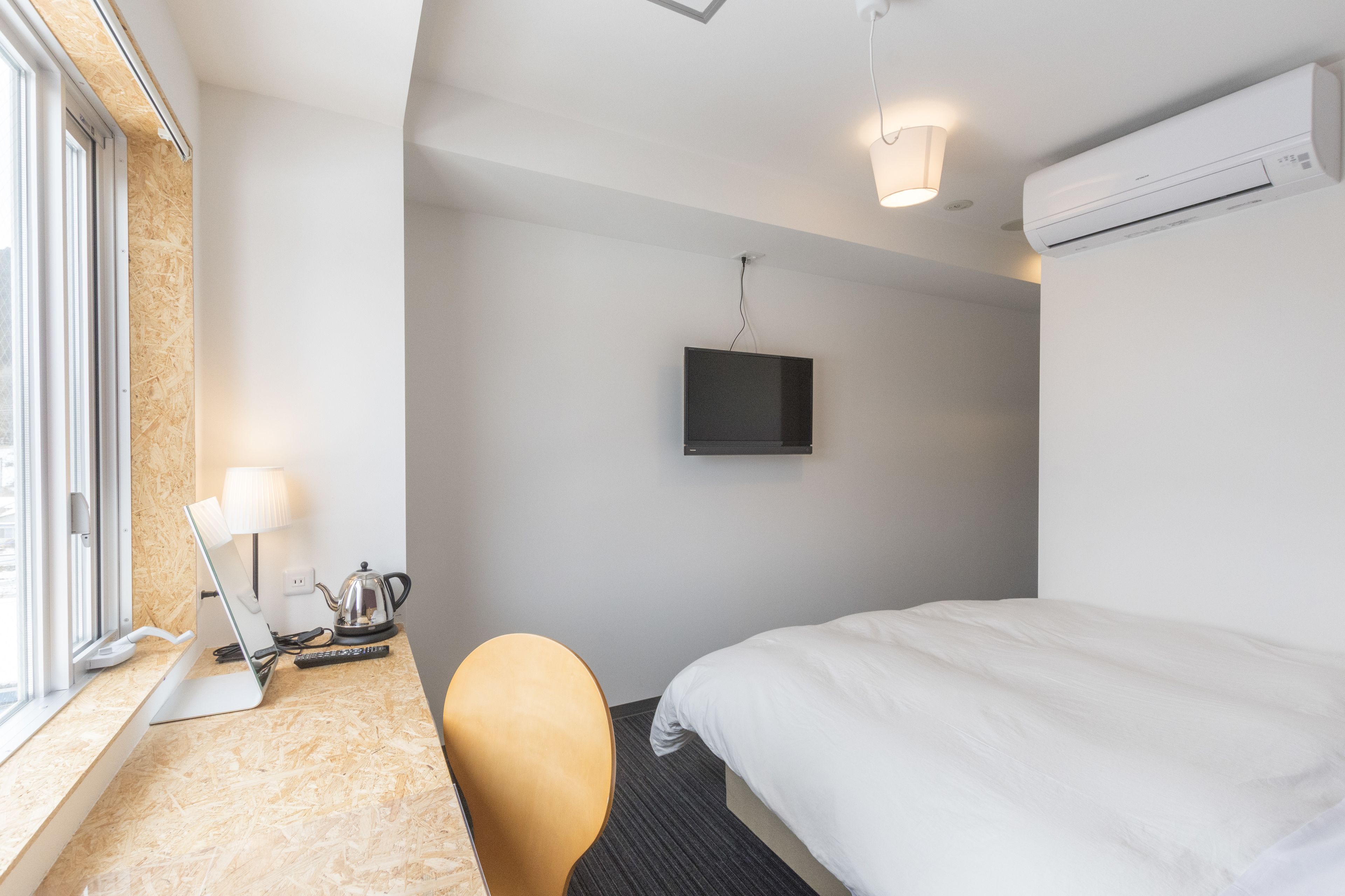 Ein Hotelzimmer mit einem Bett, einem Schreibtisch mit einem Laptop, einem Sessel, einem Fernseher und einer Klimaanlage.