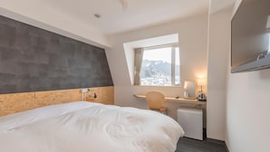 A hotel room with a large bed, a desk, a chair, a small refrigerator, a TV, and a window with a mountain view. - Nikko Station Hotel II bankan (Nikko)