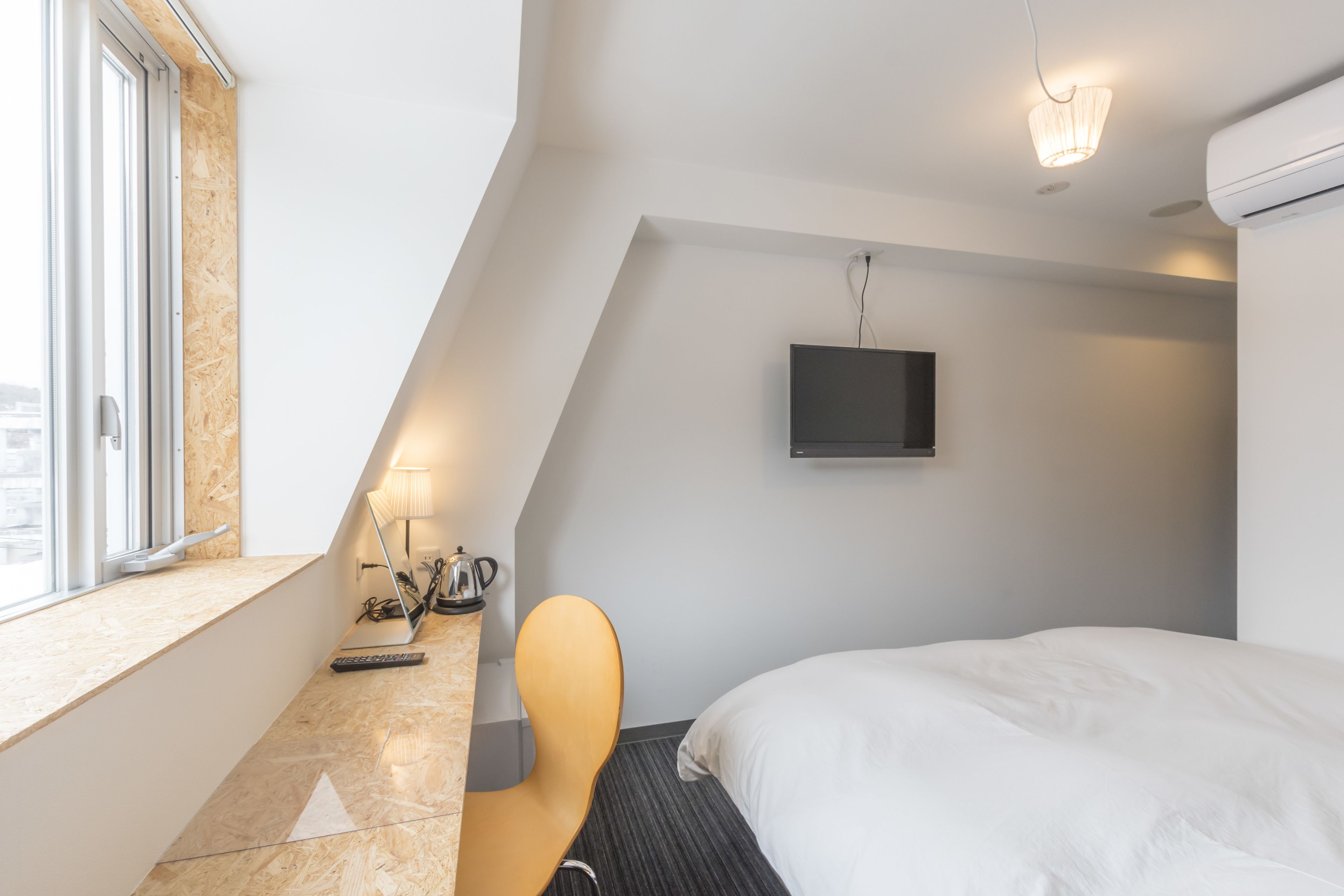Une chambre d’hôtel moderne équipée d’un lit, d’un bureau avec un ordinateur portable, d’une chaise, d’un téléviseur fixé au mur et d’une fenêtre donnant sur la ville.