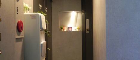 Un pasillo estrecho con un refrigerador a la izquierda, una puerta con el letrero 'VIP Room 802', y una obra de arte enmarcada en la pared.