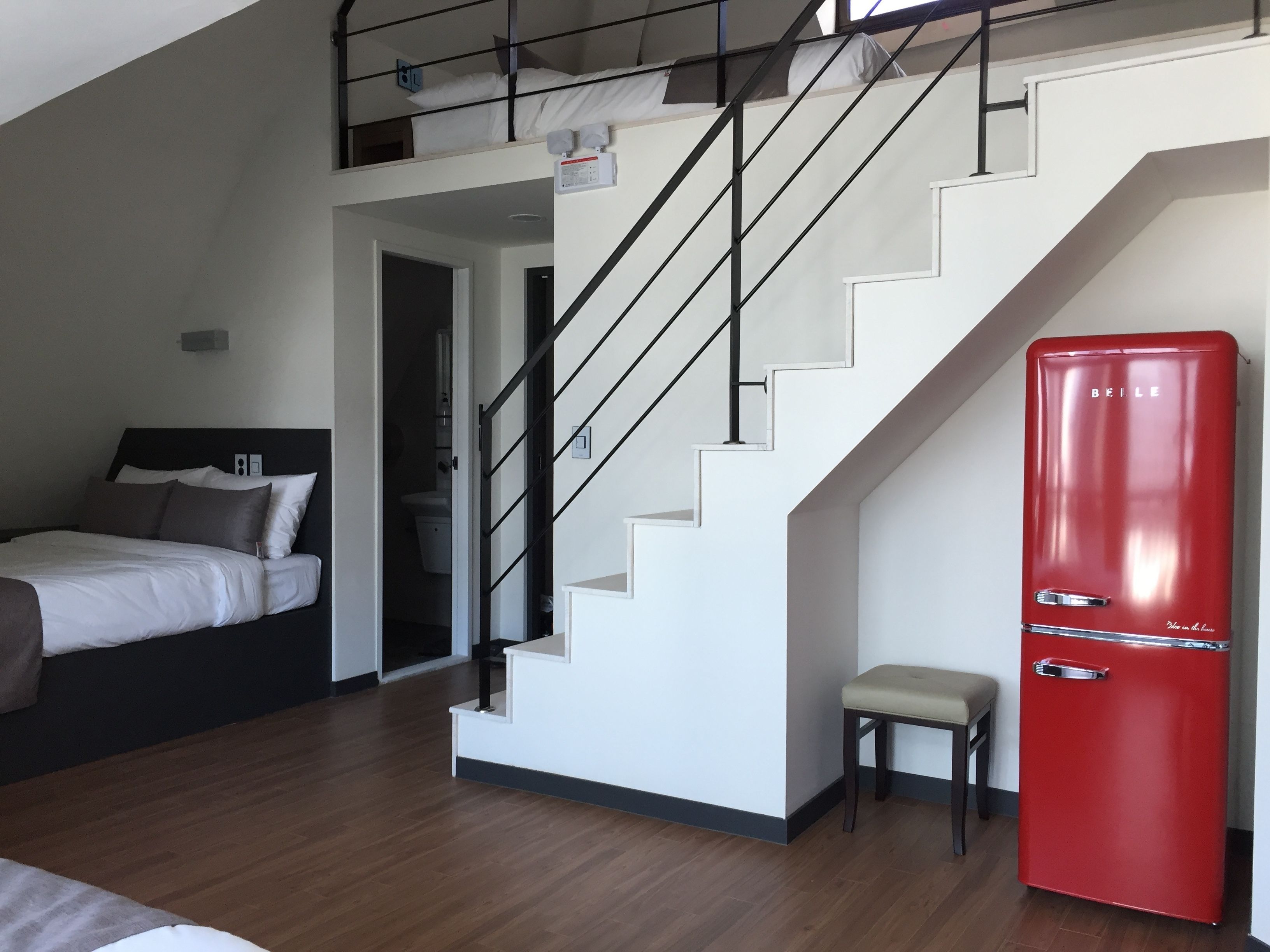 Ein Schlafzimmer mit einem Bett, einem roten Kühlschrank, einer Treppe und einem kleinen Hocker.
