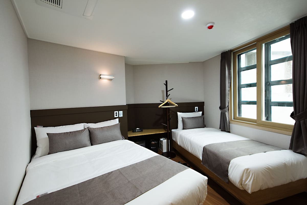A hotel room with two single beds, a bedside table, a lamp, and a window with curtains.